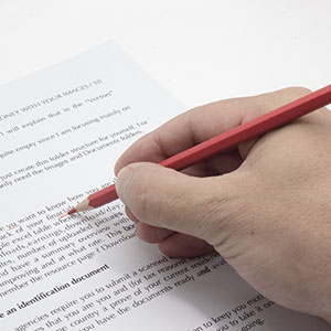 A person writing on a document with a red pencil